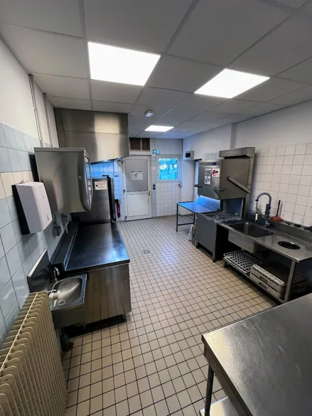 Cuisine professionnelle de la salle polyvalente équipée en inox, avec hotte d'extraction, piano de cuisson, plonge à douchette et lave-vaisselle à capot.
