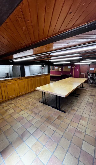 Cuisine et espace repas avec longue file de meubles en bois, éviers inox, table pliante centrale et portemanteau mural.