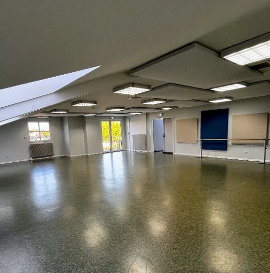 Salle des miroirs à l'étage, pièce claire sous rampants avec dalles acoustiques au plafond, barre de danse murale et porte-fenêtre donnant sur la verdure.