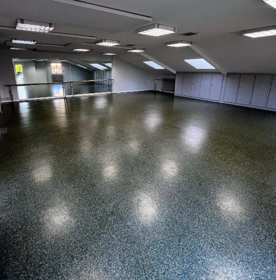 Salle des miroirs vue vers le mur de glaces et la barre de danse, sol granité brillant, velux dans les rampants et placards de rangement encastrés.