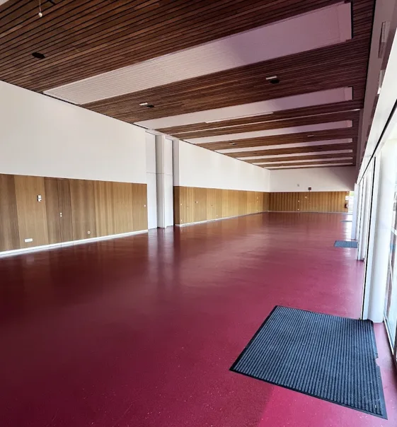 Salle rouge vue depuis l'autre extrémité, avec sol bordeaux, plafond en lattes de bois, poteaux blancs et lambris muraux.