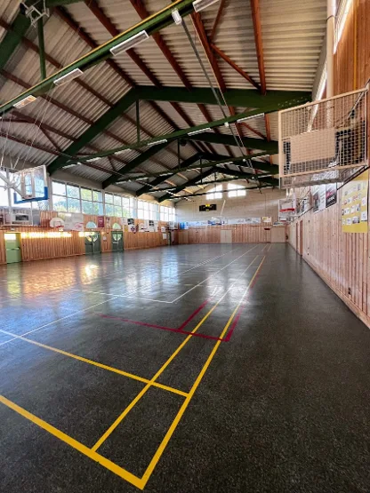 Salle verte vue depuis un angle, avec filet de protection mural, radiants de chauffage suspendus à la charpente et large surface de jeu libre de tout mobilier.