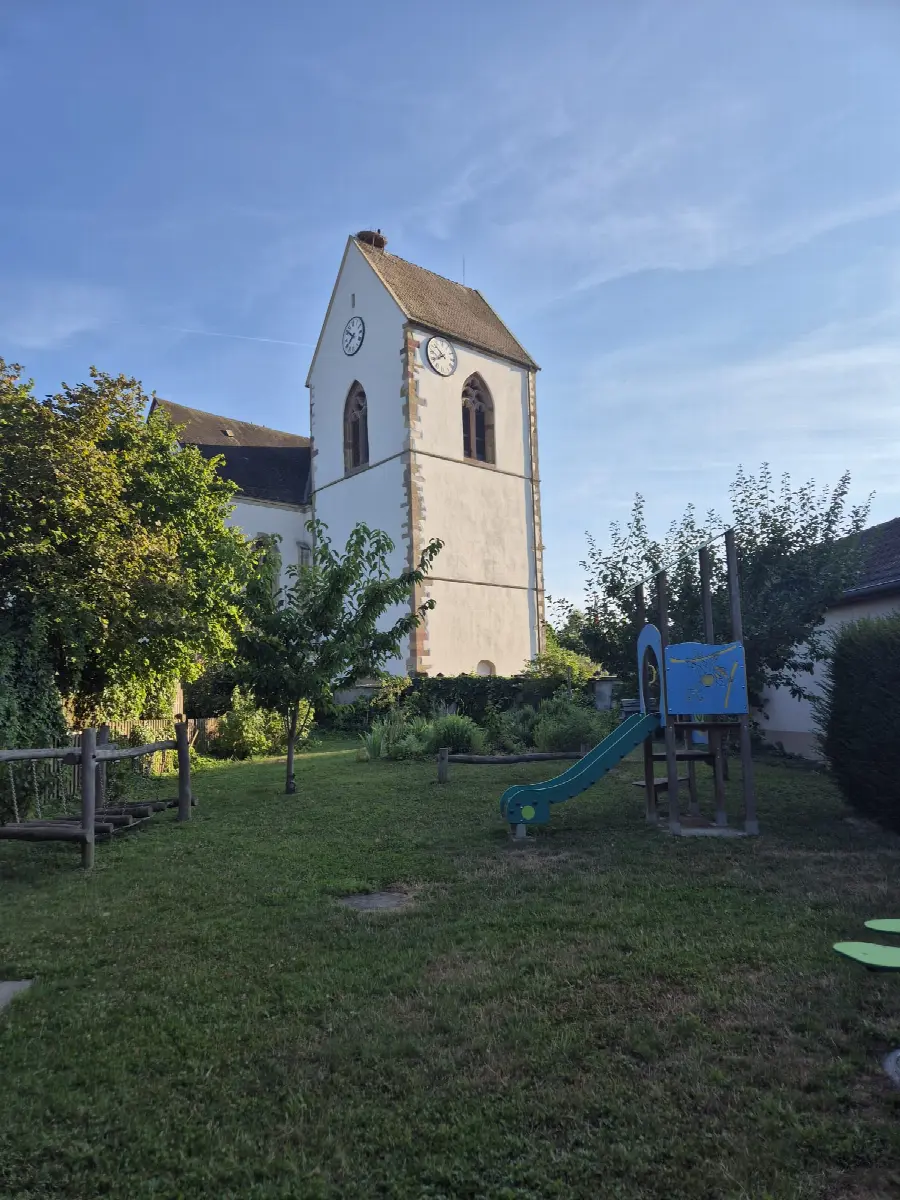 L'aire de jeux située derrière la mairie, avec un petit toboggan et le clocher de l'église en arrière-plan