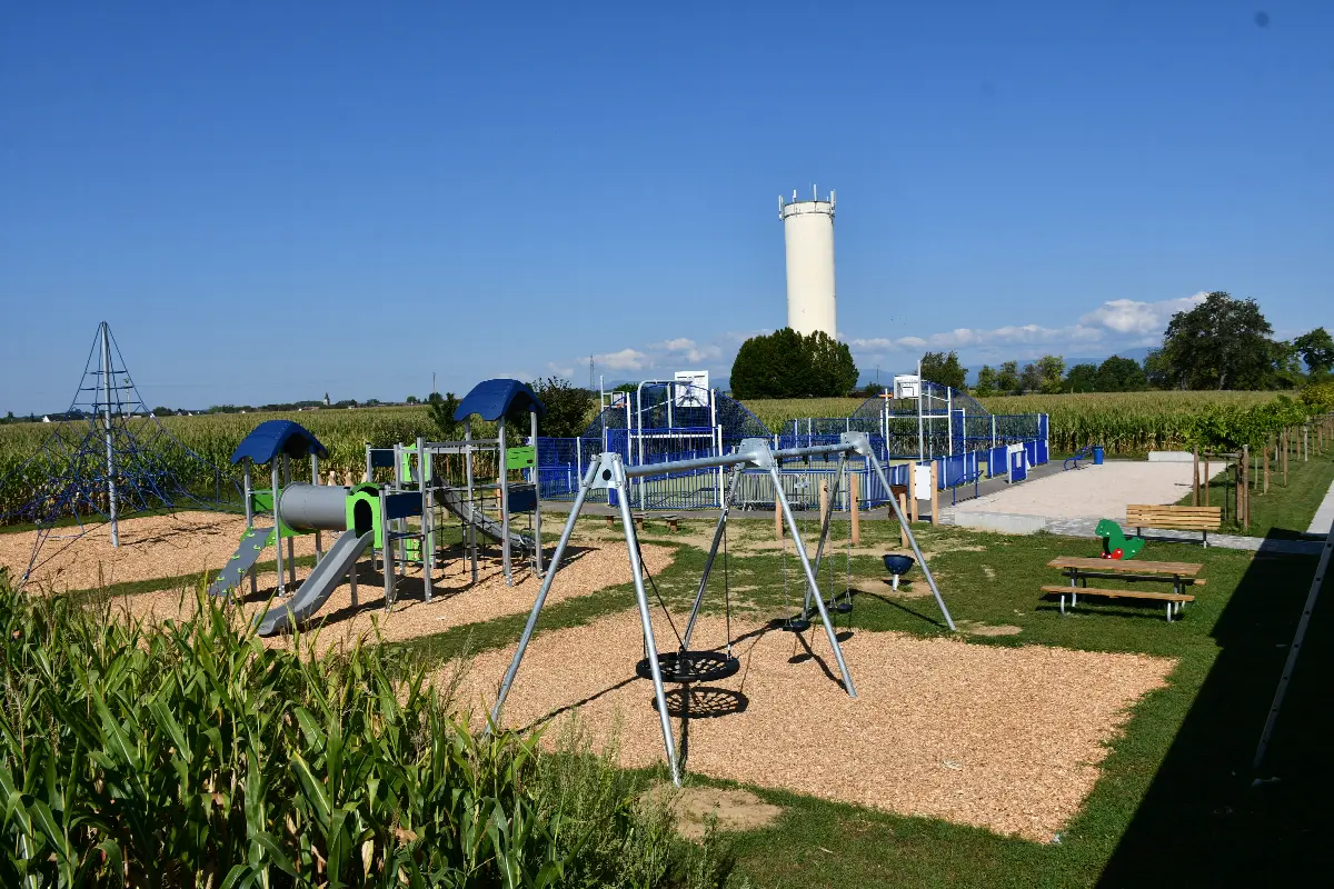L'aire de jeux de la rhubarbe : structures de jeux, balançoire et toboggan, avec le city stade et le château d'eau en arrière-plan