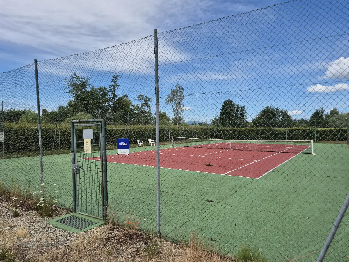 Le court de tennis de plein air de Spechbach, revêtement vert et rouge entouré d'un grillage